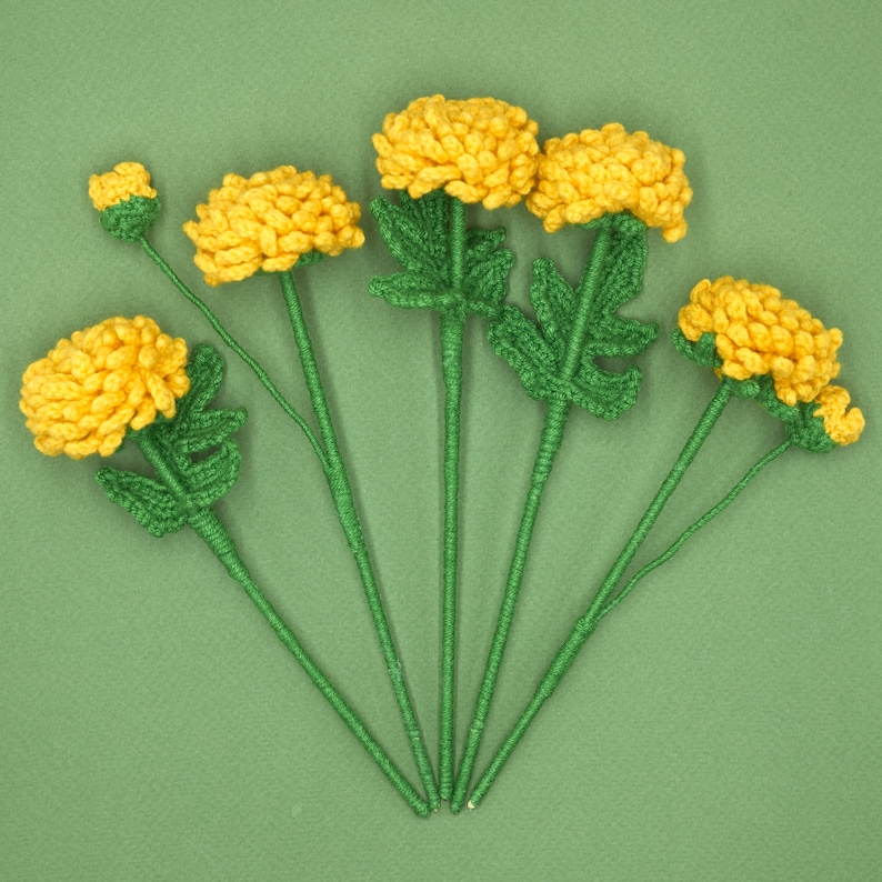 May include: A bouquet of seven crocheted yellow flowers with green stems and leaves. The flowers are arranged in a fan shape on a green background.