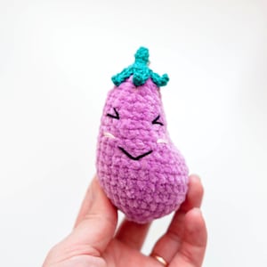 May include: A purple crocheted eggplant with a green crocheted stem and a smiling face.
