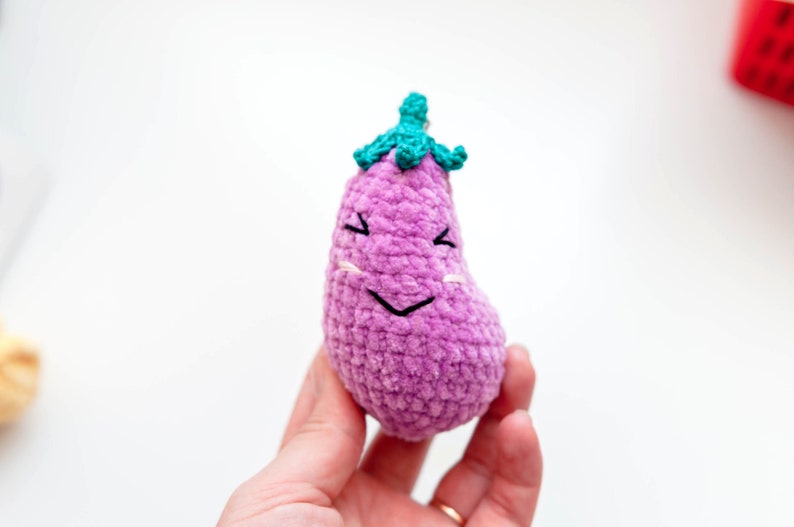 May include: A purple crocheted eggplant with a green crocheted stem and a smiling face.