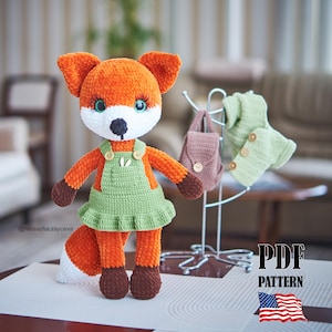 May include: A handmade orange and white fox doll with a green dress and brown accents. The fox has blue eyes and a black nose. A small backpack and sweater are on a nearby rack. The image includes the text "PDF PATTERN" and the American flag.