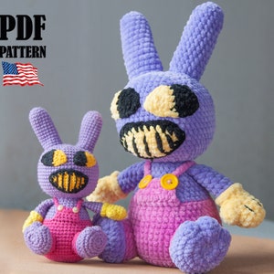 Puede incluir: Dos juguetes de peluche de conejo morado de crochet con ojos y dientes amarillos. El conejo más grande lleva un mono rosa con botones amarillos. El conejo más pequeño lleva el mismo atuendo. Los juguetes están sentados sobre una superficie marrón. PDF PATTERN.