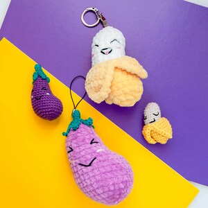May include: A set of four crocheted plush toys: a banana, an eggplant, and two smaller eggplants. The banana is yellow and has a smiling face. The eggplants are purple and have smiling faces. The banana is attached to a keychain.