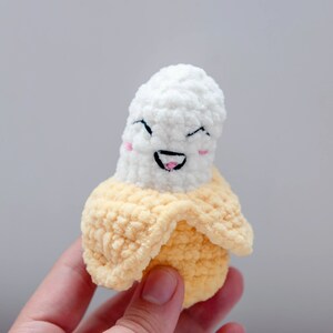 May include: A crocheted banana plush toy with a smiling face. The banana is white with a yellow peel.