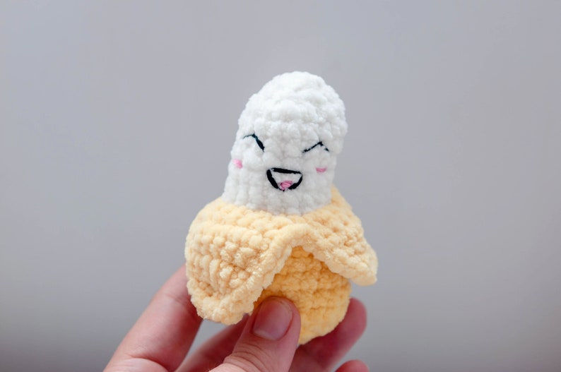 May include: A crocheted banana plush toy with a smiling face. The banana is white with a yellow peel.