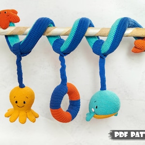 May include: A crocheted baby toy with a spiral design in blue and turquoise. The toy has three hanging attachments: a yellow octopus, an orange life preserver, and a blue whale.