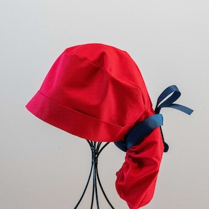 Könnte beinhalten: Eine rote OP-Haube mit einer blauen Schleife. Die Haube ist aus weichem, bequemem Stoff und hat einen gerafften Rücken.