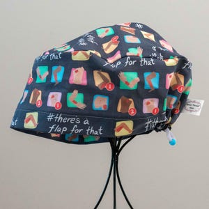 Può includere: Un berretto da lavoro nero con un motivo colorato di braccia e gambe bendate. Il berretto ha un cordoncino e il testo "#there's a flap for that" è stampato in basso.