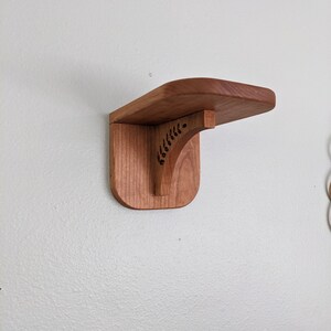 Pode incluir: Uma prateleira de madeira com um design de recorte decorativo. A prateleira est&aacute; montada em uma parede branca.