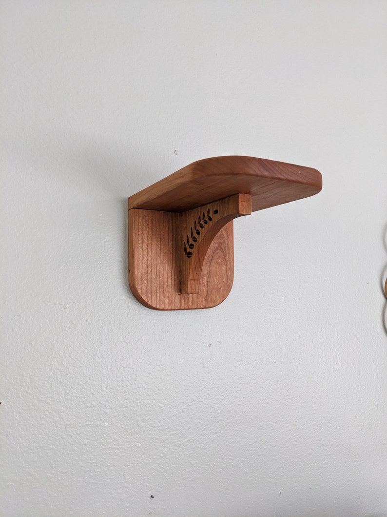 Pode incluir: Uma prateleira de madeira com um design de recorte decorativo. A prateleira est&aacute; montada em uma parede branca.