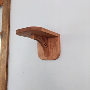 Pode incluir: Uma prateleira de madeira com um design decorativo esculpido no suporte. A prateleira est&aacute; montada em uma parede branca.