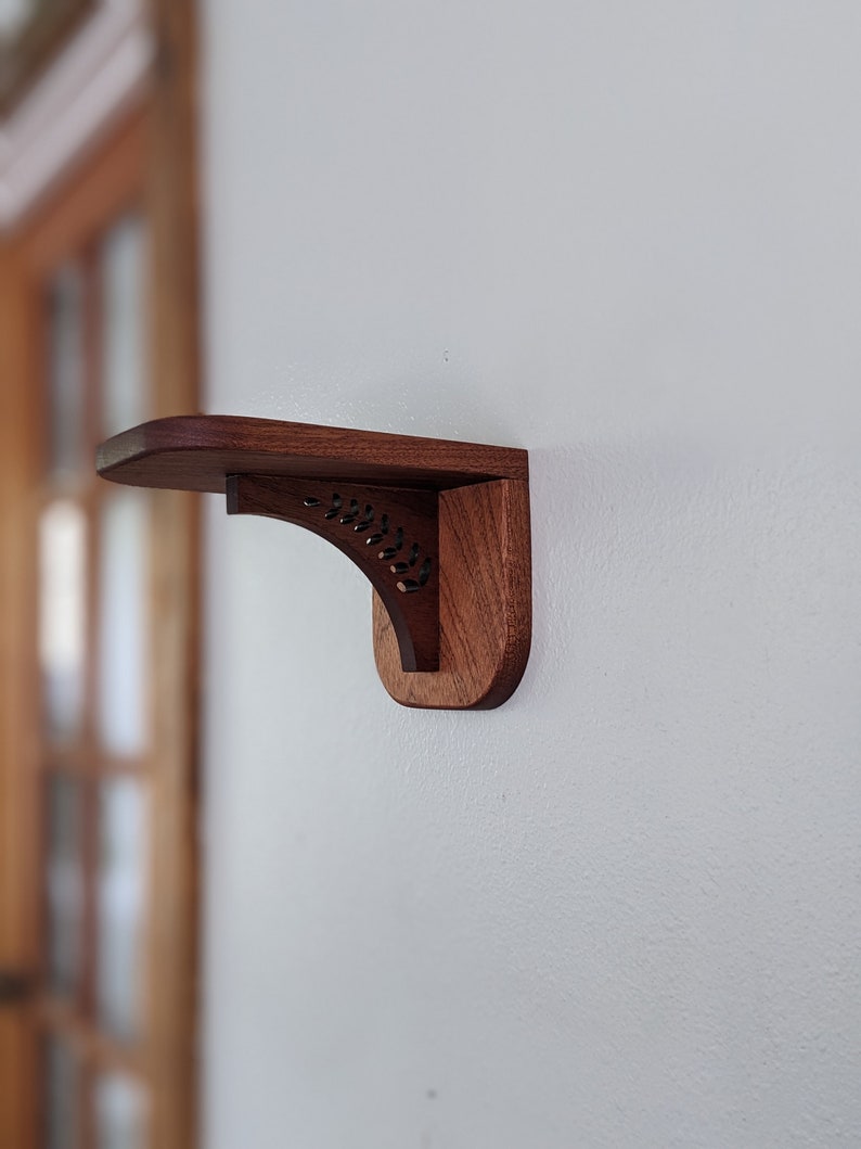 Pode incluir: Uma prateleira de madeira escura com um design de recorte decorativo est&aacute; montada em uma parede branca.