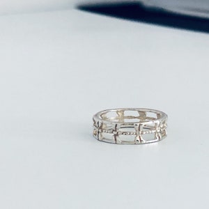 May include: A silver ring with a geometric design. The ring is made of a thin band with a series of open squares and rectangles.