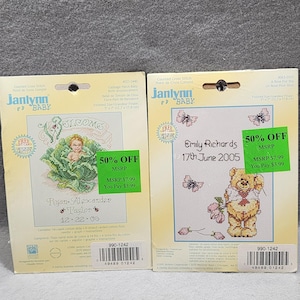 Könnte beinhalten: Zwei Kreuzstich-Sets von Janlynn Baby. Eines zeigt ein Baby in einem Kohlkopf mit dem Namen "Ryan-Alexander Taylor" und dem Datum 12-22-06. Das andere zeigt einen Teddybären mit dem Namen "Emily Richards" und dem Datum 17. Juni 2005. Beide Sets sind 50% reduziert.