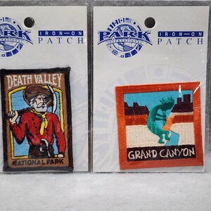May include: Two rectangular embroidered iron-on patches on white backing cards. The left patch depicts a prospector with a pickaxe and the text Death Valley National Park. The right patch shows a turquoise Kokopelli figure and Grand Canyon text.