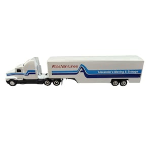 May include: A white toy semi-truck with a trailer featuring blue and light blue stripes. The text Atlas Van Lines is printed in red and black, and Alexander's Moving & Storage is printed in blue on the side of the trailer with a large blue letter A.