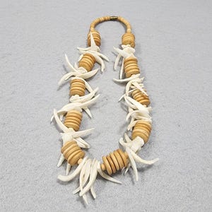 May include: A necklace featuring alternating segments of light brown, cylindrical wooden beads and clusters of curved, off-white, horn-like pieces. The necklace is secured with a small, metallic, cylindrical clasp at the top center of the strand.