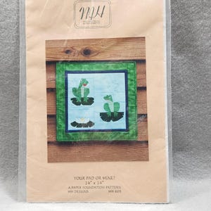 May include: A paper foundation quilt pattern titled Your Pad or Mine? by MH Designs, model MH 603. The packaging features a 14 inch by 14 inch square quilt design showing green frogs on lily pads against a light blue background with a green border.