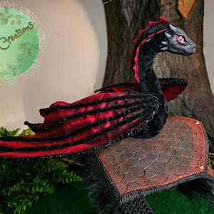 Puede incluir: Un juguete de peluche de dragón negro y rojo con una espalda texturizada, marrón y escamosa. El dragón tiene un cuello largo y una cabeza pequeña y puntiaguda con ojos rojos.