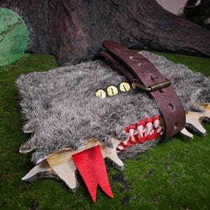 Può includere: Un diario fatto a mano a tema fantasy con una copertina in finta pelliccia, progettato per assomigliare a un mostro. Il diario presenta un cinturino in pelle marrone, dettagli occhi dorati e un segnalibro rosso a forma di lingua.