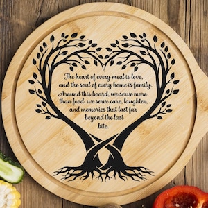May include: A round wooden serving board with a handle, featuring a heart-shaped tree design and the text "The heart of every meal is love..." in black. The board is surrounded by fresh vegetables, including a red bell pepper, and a knife.