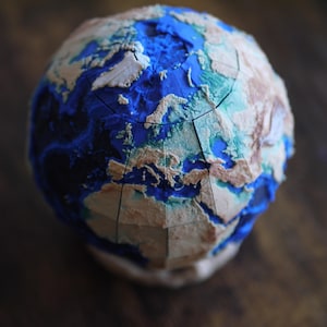 以下が含まれることがあります： 詳細な、3次元の地球儀モデル。表面はテクスチャ加工が施され、大陸はベージュと茶色で、海は青色で表現されています。地球儀はセグメント化されており、ユニークで芸術的なデザインを示しています。