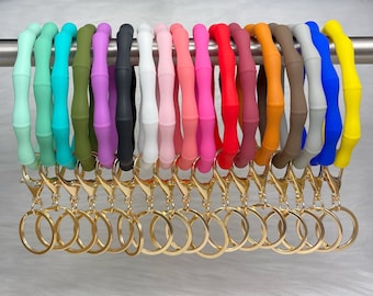 May include: A set of 15 colorful silicone keychains with gold key rings. The keychains are shaped like a bamboo ring and come in a variety of colors, including blue, green, purple, pink, red, orange, yellow, and brown.
