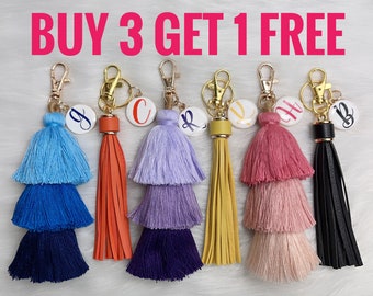 May include: Buy 3 get 1 free.  Set of six colorful tassel keychains with a round charm featuring a letter.  The charms are attached to a gold-colored metal ring.  The tassels are made of multi-colored yarn and are layered in three tiers.