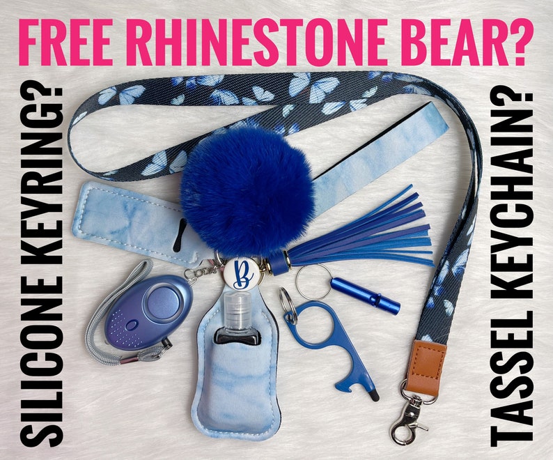 May include: A blue and black patterned lanyard with a blue pom-pom tassel, a blue silicone keychain with a hand sanitizer holder, a blue personal alarm, a blue and silver key ring, and a blue and silver tool. The lanyard has the text "FREE RHINESTONE BEAR?" and "TASSEL KEYCHAIN?" on it. The text "SILICONE KEYRING?" is on the left side of the image.