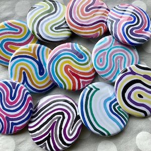 May include: A selection of circular buttons with a vibrant, swirled pattern. The buttons display a range of colours, such as blue, green, yellow, red, purple, and pink. The buttons are arranged in a random pattern.