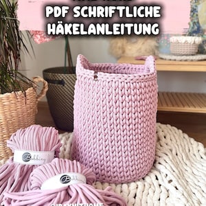Peut inclure: Un grand panier tricoté rose clair avec des poignées, à côté de plusieurs écheveaux de fil assorti. Le fil porte des étiquettes blanches avec la marque "Bobbiny". Le texte "XXL KORB PDF SCHRIFTLICHE HÄKELANLEITUNG" est en haut de l'image.