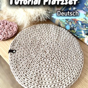 以下が含まれることがあります： ベージュ色の円形プレースマット。厚手の織り素材で、スパイラル模様が施されています。画像には、小さなピンク色のコースターと「Tutorial Platzset Deutsch」というテキストも表示されています。プレースマットは木製の表面にあります。