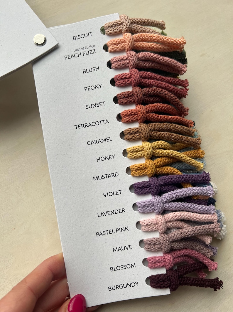 Op de afbeelding: Een kleurenkaart met 15 verschillende tinten garen, waaronder Biscuit, Peach Fuzz, Blush, Pioenroos, Zonsondergang, Terracotta, Karamel, Honing, Mosterd, Violet, Lavendel, Pastelroze, Mauve, Bloesem en Bourgondi&euml;.