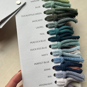 Op de afbeelding: Een kleurenkaart met 14 verschillende tinten garen, waaronder matcha, alo&euml;, eucalyptusgroen, avocado, laurier, teal, pauwblauw, eendeneiblauw, mistig, perfect blauw, jeans, iris en maanlicht.