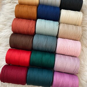 Könnte beinhalten: Sortiment von 16 Spulen mit farbigem geflochtenem Kordel. Die Kordeln sind in zwei Reihen zu je acht angeordnet, wobei jede Reihe eine andere Farbe aufweist. Die Farben umfassen Beige, Braun, Rot, Dunkelbraun, Grün, Blau, Hellblau, Grau, Schwarz, Weiß, Rosa und Lila.