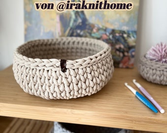 Puede incluir: Dos cestas de crochet beige, una más grande que la otra, en un estante de madera. La cesta más grande tiene un asa de cuero marrón. El texto "Video Anleitung Runder Korb/ Katzen Korb von @iraknithome" es visible sobre las cestas.