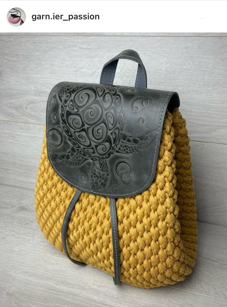 May include: A yellow crocheted backpack with a black leather flap featuring an embossed turtle design. The backpack has a top handle and adjustable straps.