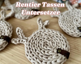 Puede incluir: Posavasos de ganchillo beige en forma de reno con detalles de cuero marrón. Los posavasos están sobre una superficie de madera. Video Anleitung Rentier Tassen Untersetzer @iraknithome