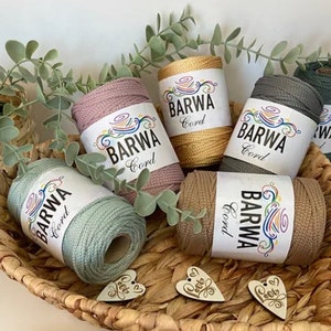 Könnte beinhalten: Fünf Spulen mit farbigem Baumwollgarn in einem Weidenkorb. Die Spulen sind mit "Barwa Cord" beschriftet und in den Farben Rosa, Beige, Grün, Grau und Gelb.