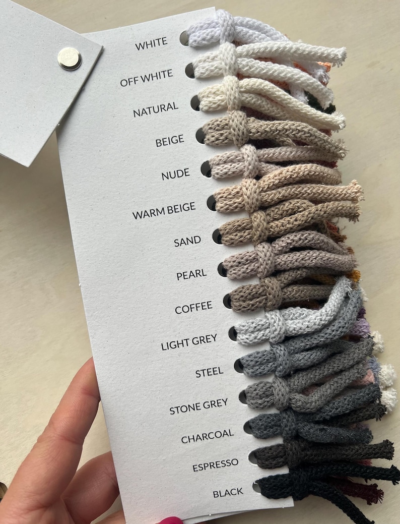 Op de afbeelding: Een kleurenkaart met 15 verschillende tinten koord, vari&euml;rend van wit tot zwart. Het koord is verticaal gerangschikt, met de lichtste tint bovenaan en de donkerste tint onderaan. De kleurennamen zijn afgedrukt aan de linkerkant van de kaart.