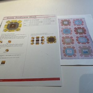 May include: A printed pattern for a "Sunny Sunflower Block" quilt. The instructions are on the left, with a diagram of the block and a sample quilt on the right. The sample quilt has six blocks with various designs in shades of blue, pink, and orange.