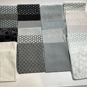 May include: A collection of square fabric swatches arranged in a grid, featuring various shades of black, gray, and white. The patterns include geometric shapes, circles, dots, and floral motifs printed on the textile surfaces.