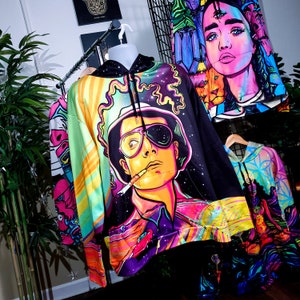 May include: A black hooded sweatshirt with a colorful psychedelic print featuring a man with sunglasses and a cigarette. The print includes a galaxy background and a spaceship.