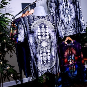 May include: Three different shirts with geometric patterns. The shirt in the center has a white and black geometric pattern with a mandala design. The shirt on the left has a colorful galaxy pattern. The shirt on the right has a colorful geometric pattern with a rainbow color scheme.