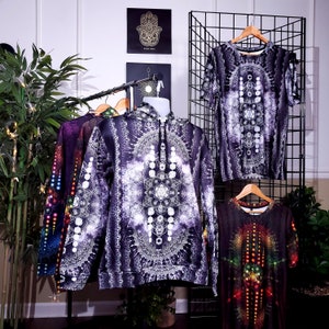 Puede incluir: Cinco prendas de vestir diferentes en estantes de exhibición. La ropa es de color negro y blanco con intrincados patrones geométricos. La ropa incluye una sudadera con capucha, una camisa de manga larga y tres camisas de manga corta.