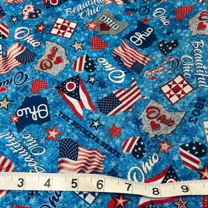 May include: Blue fabric with a pattern featuring Ohio state flags, hearts, stars, and the words "Ohio" and "Beautiful Ohio." A measuring tape shows inches. The Buckeye State theme is prominent.