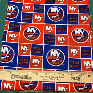 May include: A blue and orange fabric with a repeating pattern of the New York Islanders hockey team logo. The logo features a hockey stick and puck with the words "New York Islanders" and "NY" in a circle.