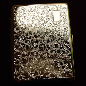 May include: A silver cigarette case with an ornate floral design.