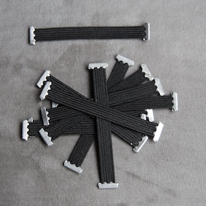May include: A bundle of black elastic bands with silver metal clasps. The bands are arranged in a starburst pattern.
