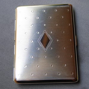 May include: Silver cigarette case with a diamond pattern and a star design.