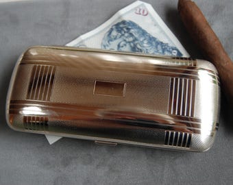 Peut inclure: Un étui à cigarettes en argent avec une surface texturée et un motif décoratif. L'étui a un couvercle à charnière et un petit loquet.